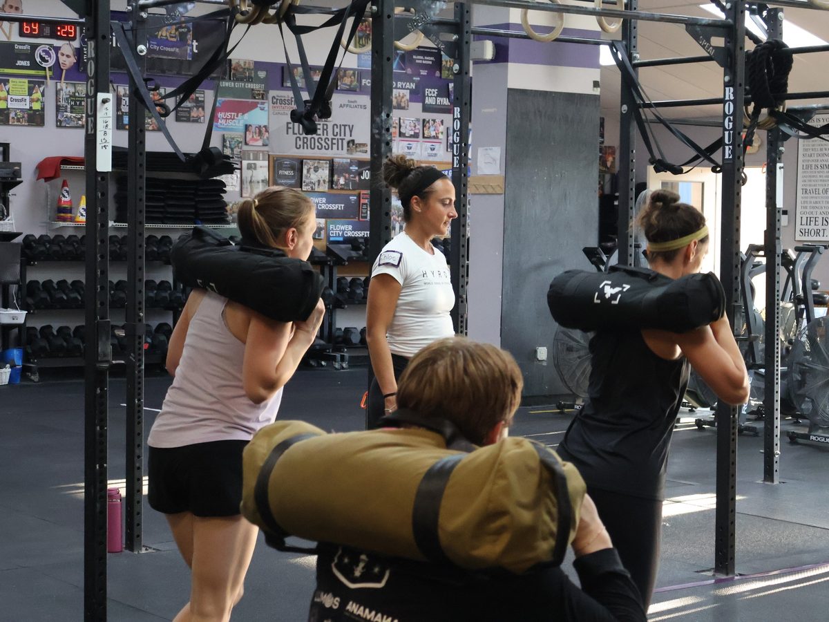 A coach guiding members through sandbag work at Flower City CrossFit